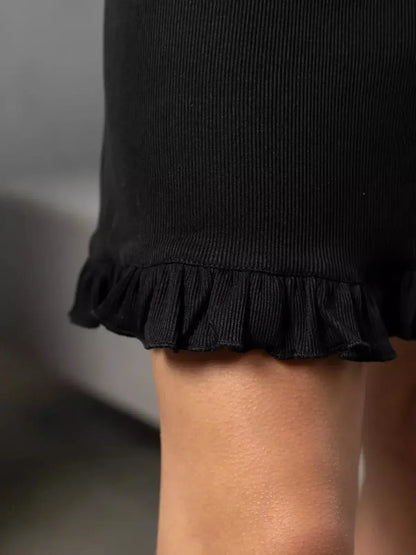Close-up of the ruffled hem of the Noir Flare black mini dress, showcasing its elegant detailing and soft ribbed texture.