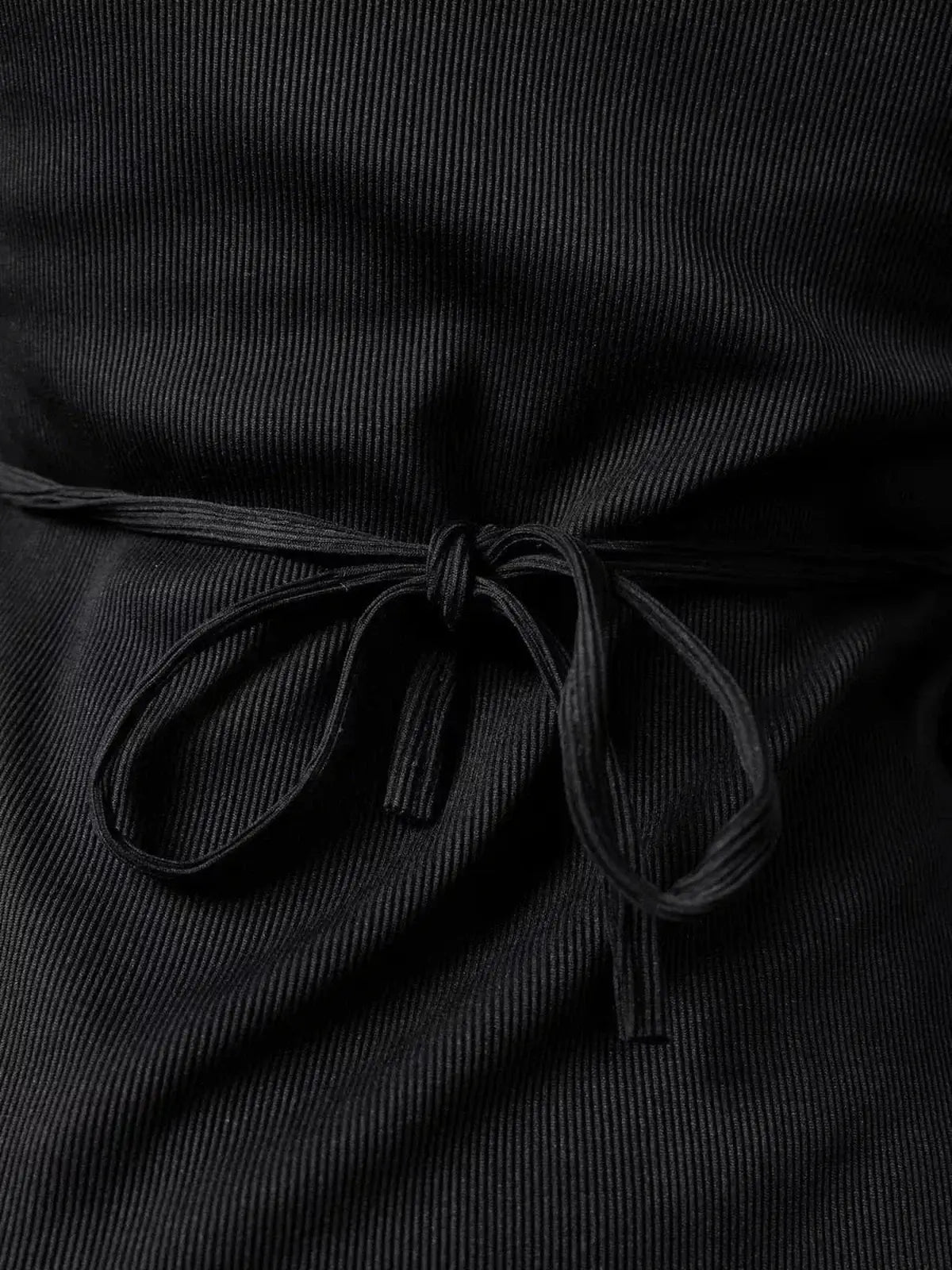 Close-up of lace-up detail on a black ribbed mini dress showcasing elegance and style.