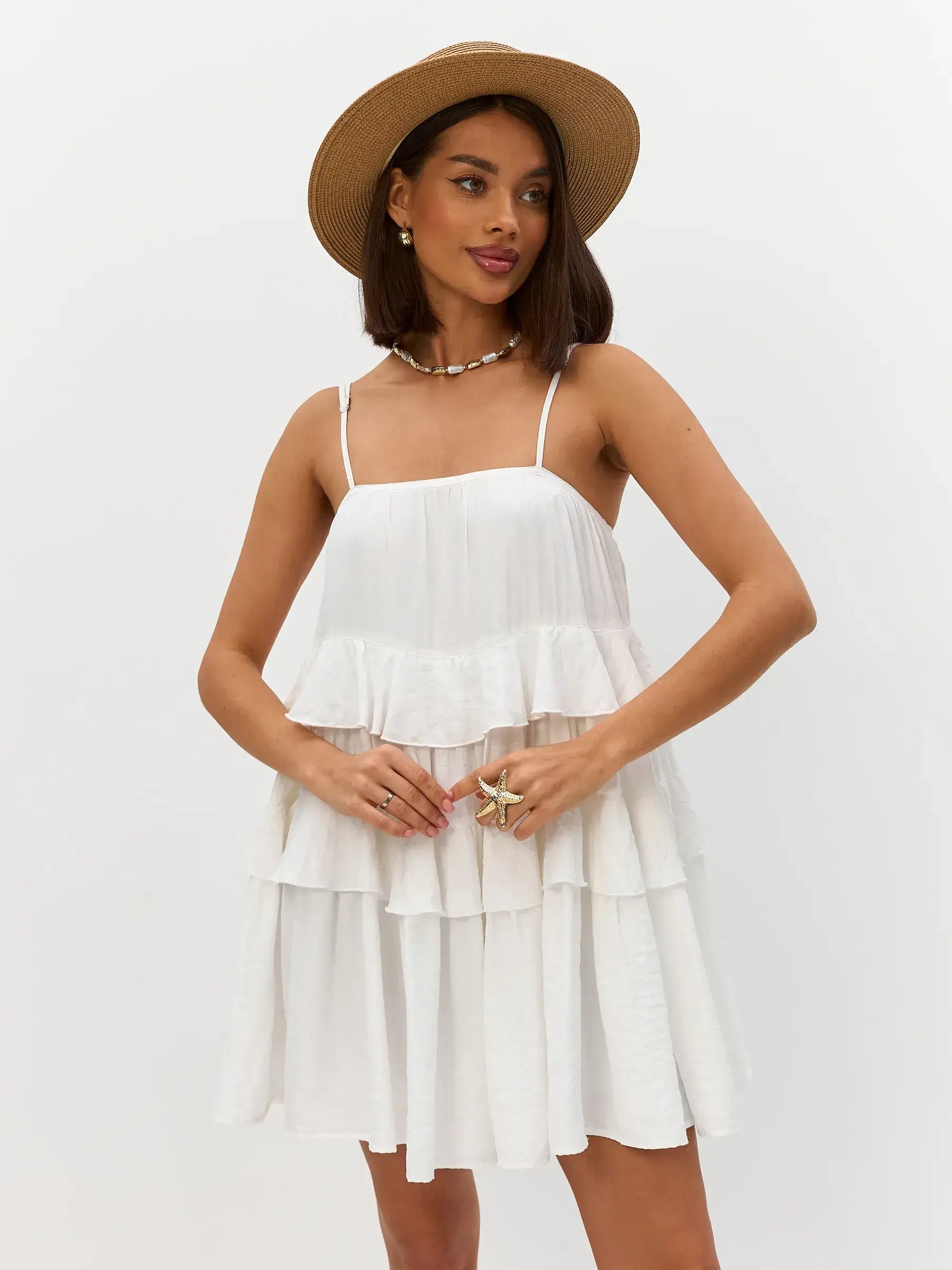 Model wearing the Riviera Ruffle white summer dress with ruffles and a floppy hat, perfect for weddings or casual outings.