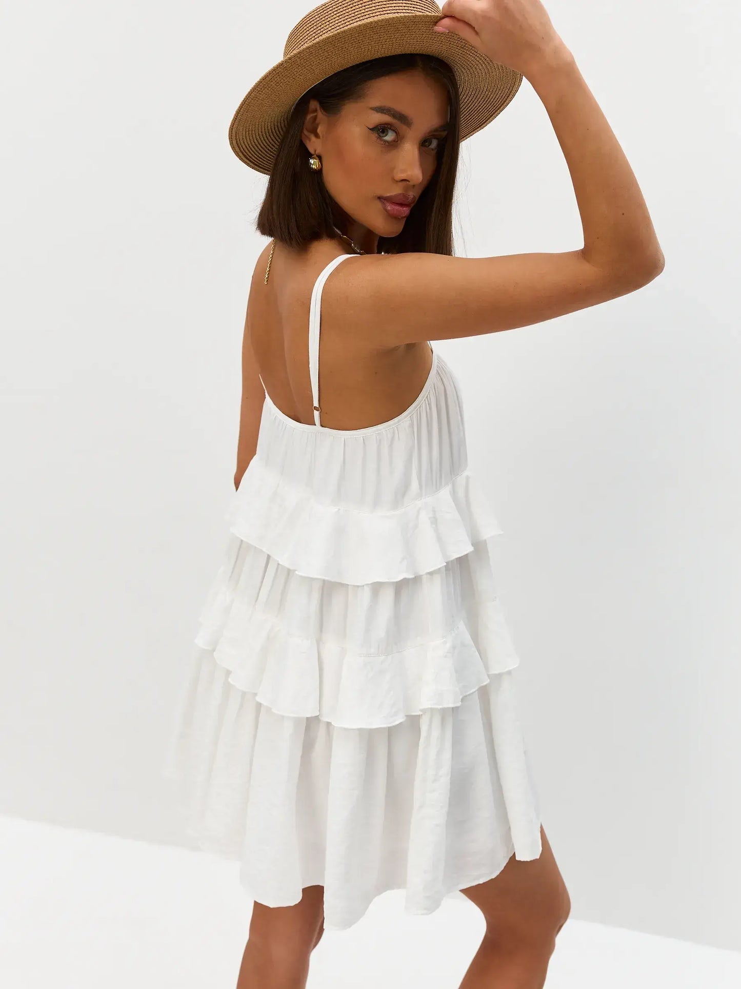 Model wearing the Riviera Ruffle white mini dress with tiered ruffles and a straw hat for a summer look.