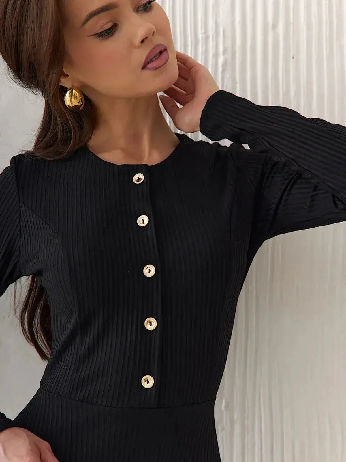 Close-up of a woman in a black ribbed midi dress featuring golden buttons, showcasing elegant women's clothing.