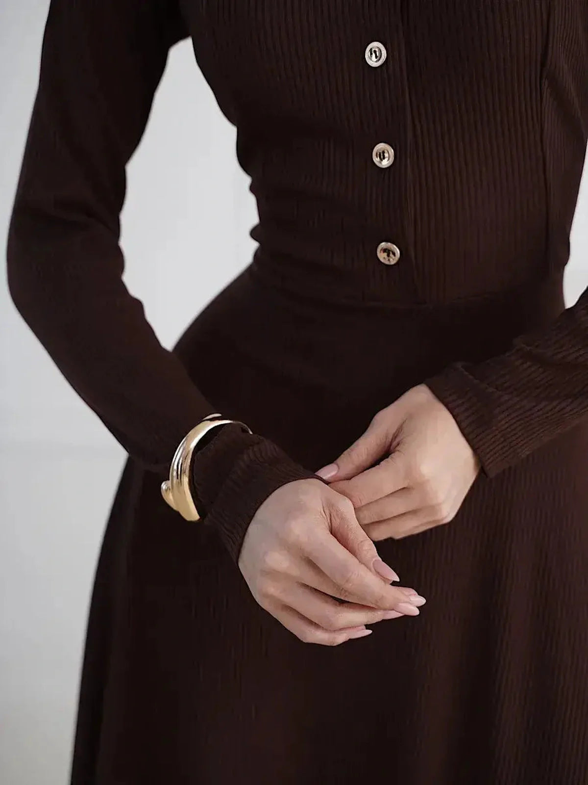 Close-up of a woman in a brown midi dress featuring button detailing and a stylish cuff, showcasing elegant fashion for various occasions.