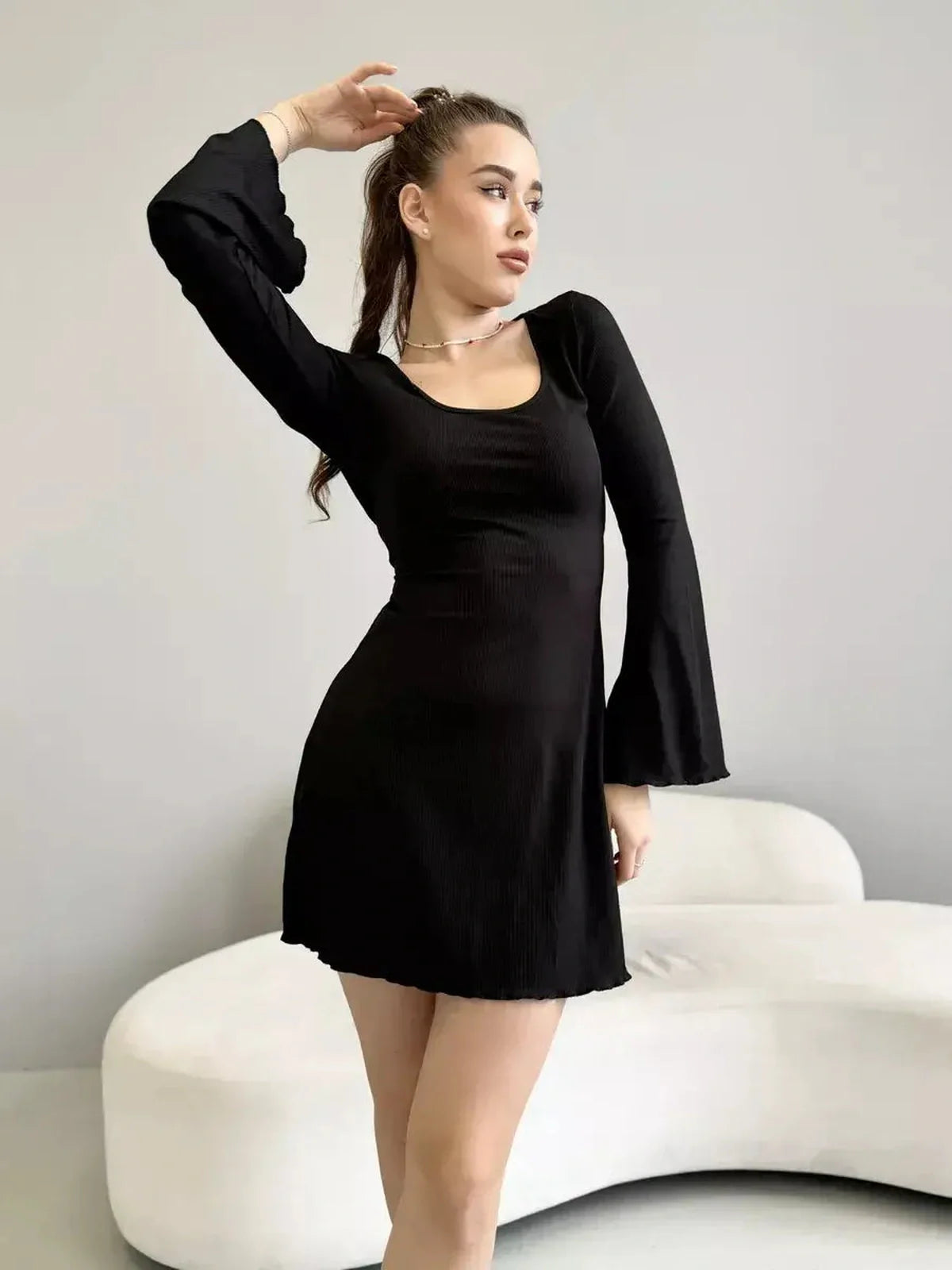 Model showcasing the Noir Flare black mini dress with flared sleeves and a deep square neckline.