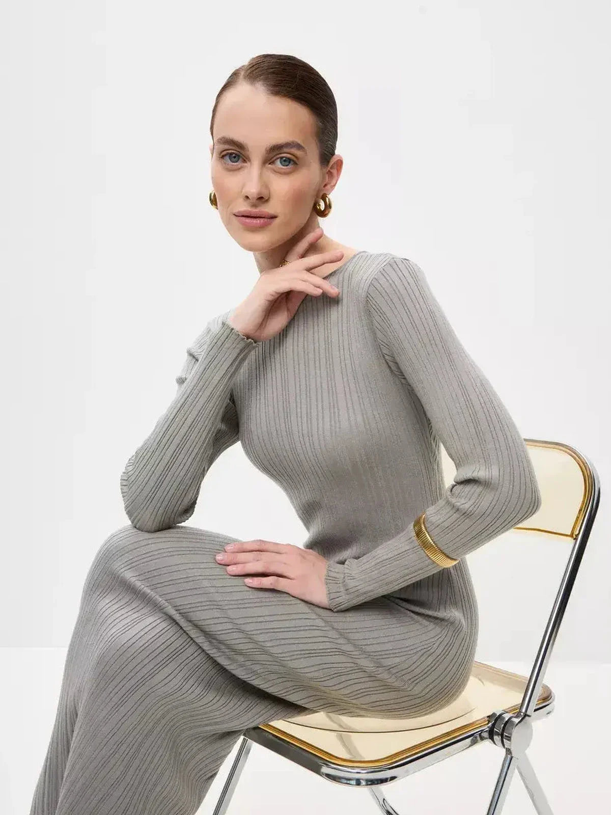 Stylish woman in a ribbed gray Sculpted Grace Maxi Dress seated on a chair, showcasing elegance and comfort.