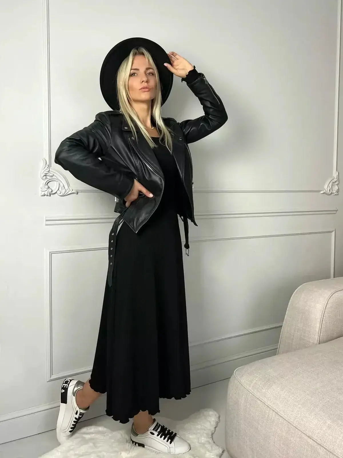 Woman in a black midi dress with a leather jacket and hat, showcasing a chic and casual style.