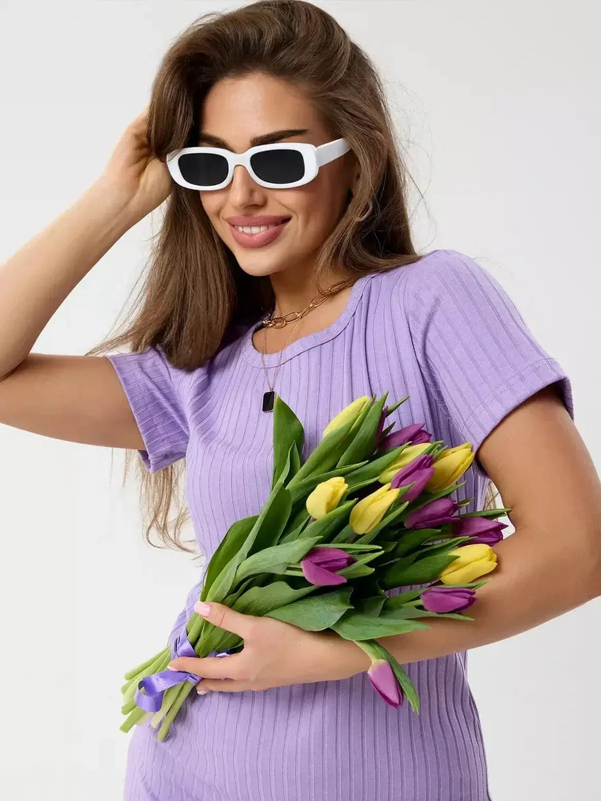Woman in a lilac mini dress holding a bouquet of colorful tulips, showcasing a stylish summer look with bold sunglasses.