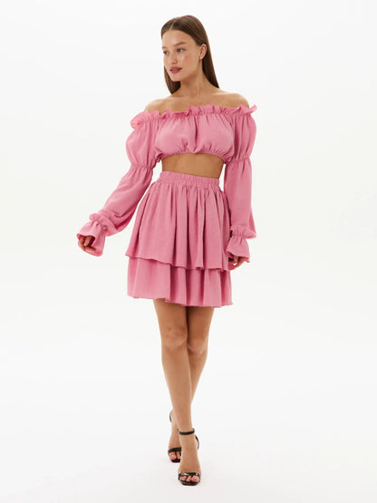 Stylish pink tiered ruffle set featuring an off-shoulder crop top and layered mini skirt, perfect for summer events.