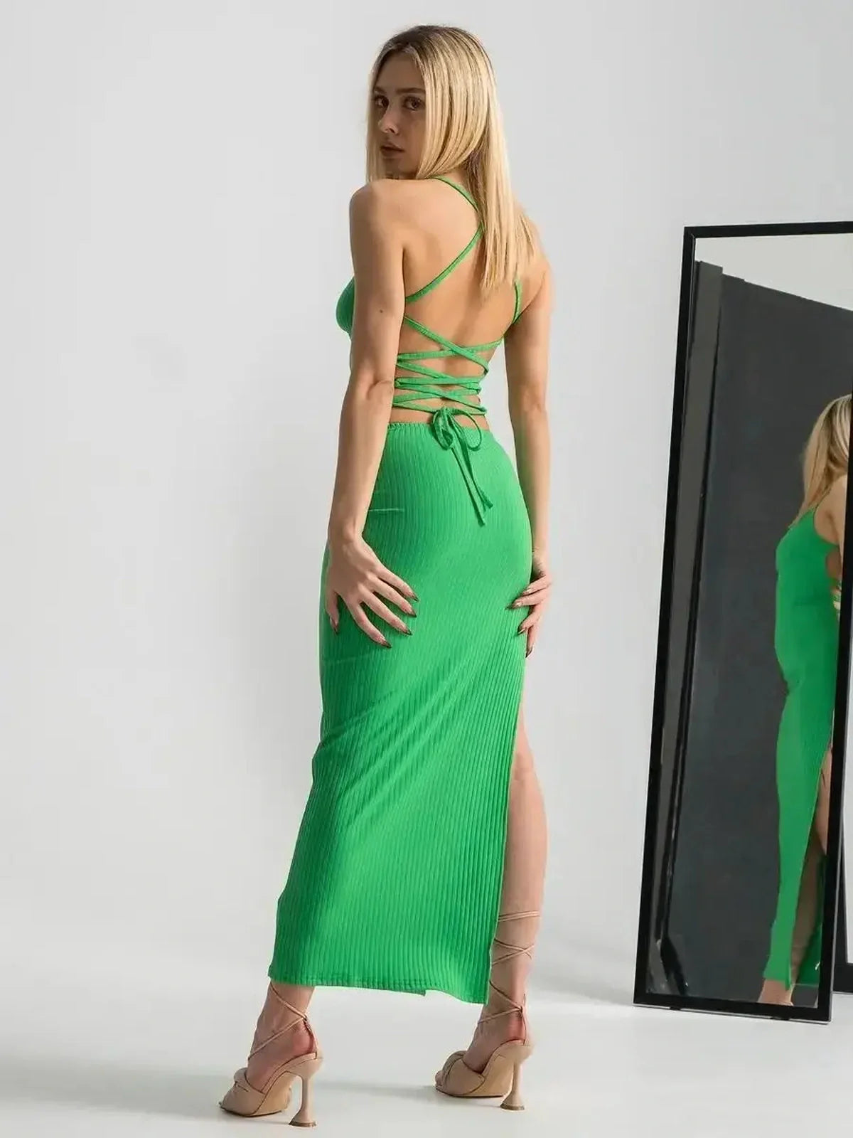 Back view of a woman in a vibrant green maxi dress with a strappy back and leg slit, ideal for summer occasions.