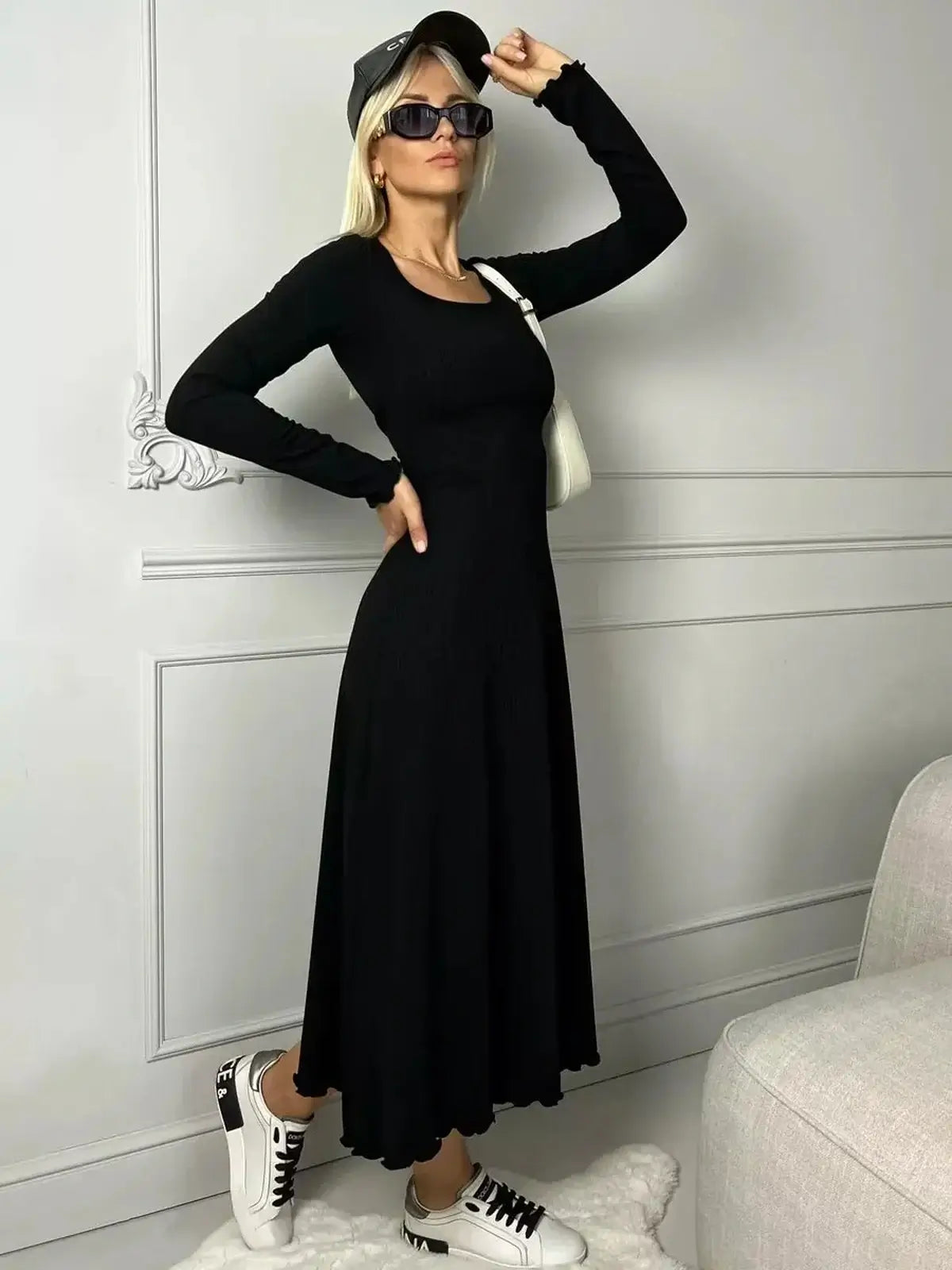 Model showcasing the Sculpted Grace Midi Dress in black, featuring a flared silhouette and long sleeves, paired with sneakers.