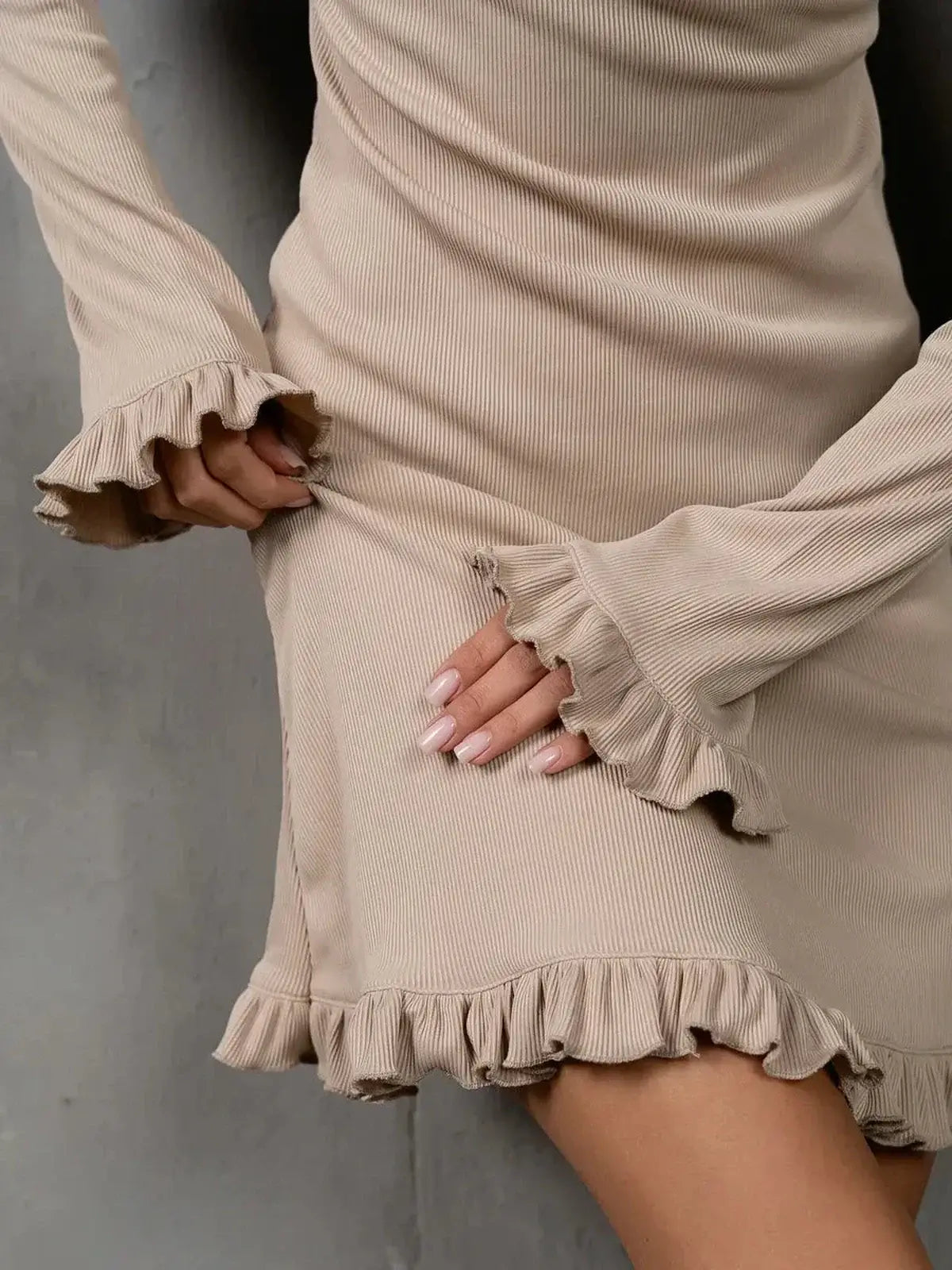 Close-up of a woman in a beige Luna Flare dress with ruffle accents at the hem and sleeves, showcasing soft elegance.