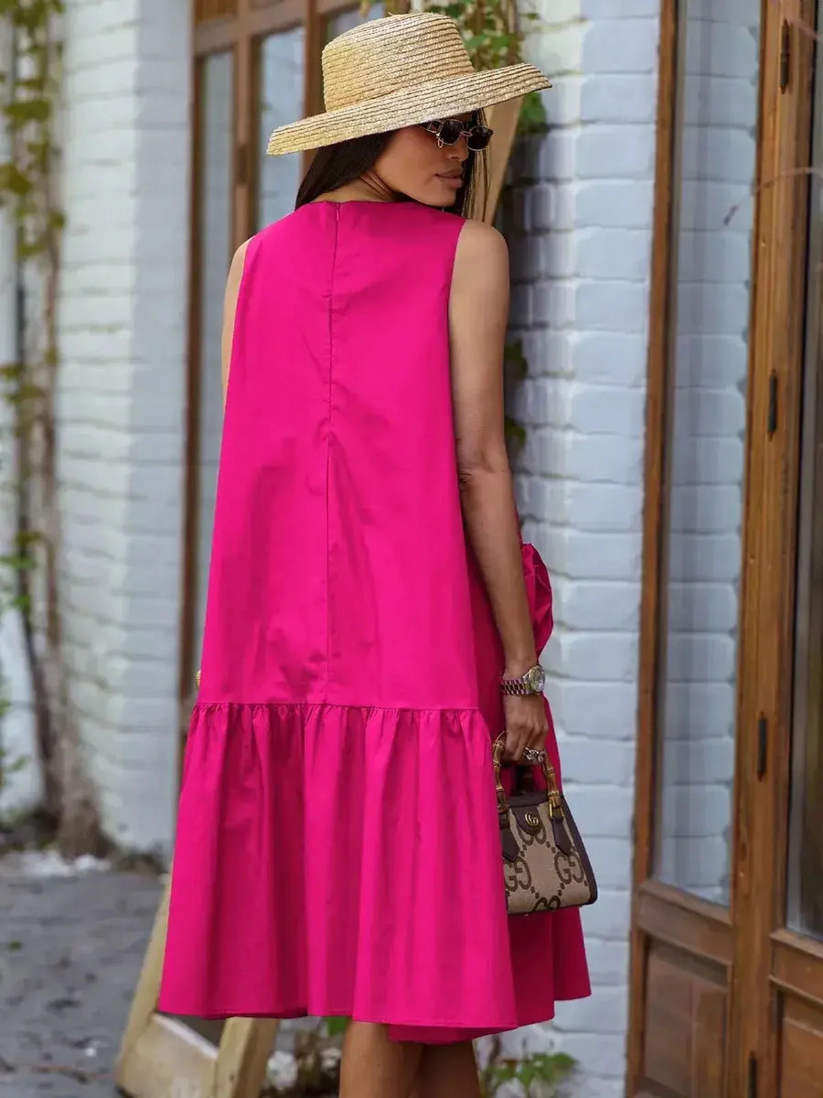 Bold fuchsia midi dress featuring tiered hem and oversized rosette accents, perfect for summer occasions.