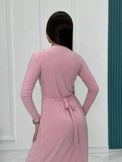 Back view of a woman in a powder pink eclipse maxi dress with long sleeves and adjustable waist tie.