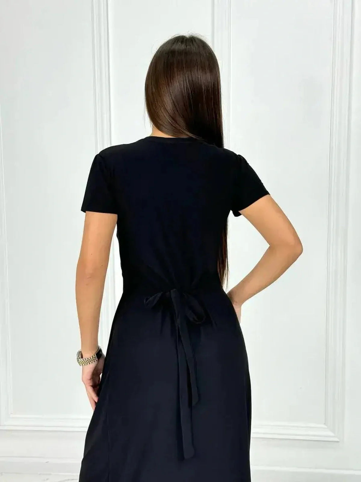 Back view of a woman wearing an elegant black maxi dress with a tie detail, perfect for casual summer styling.