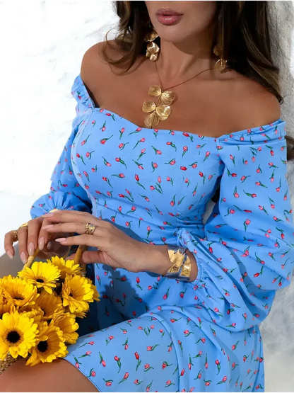 Model wearing the Sky Petals mini dress with floral prints, holding sunflowers, showcasing summer style and femininity.