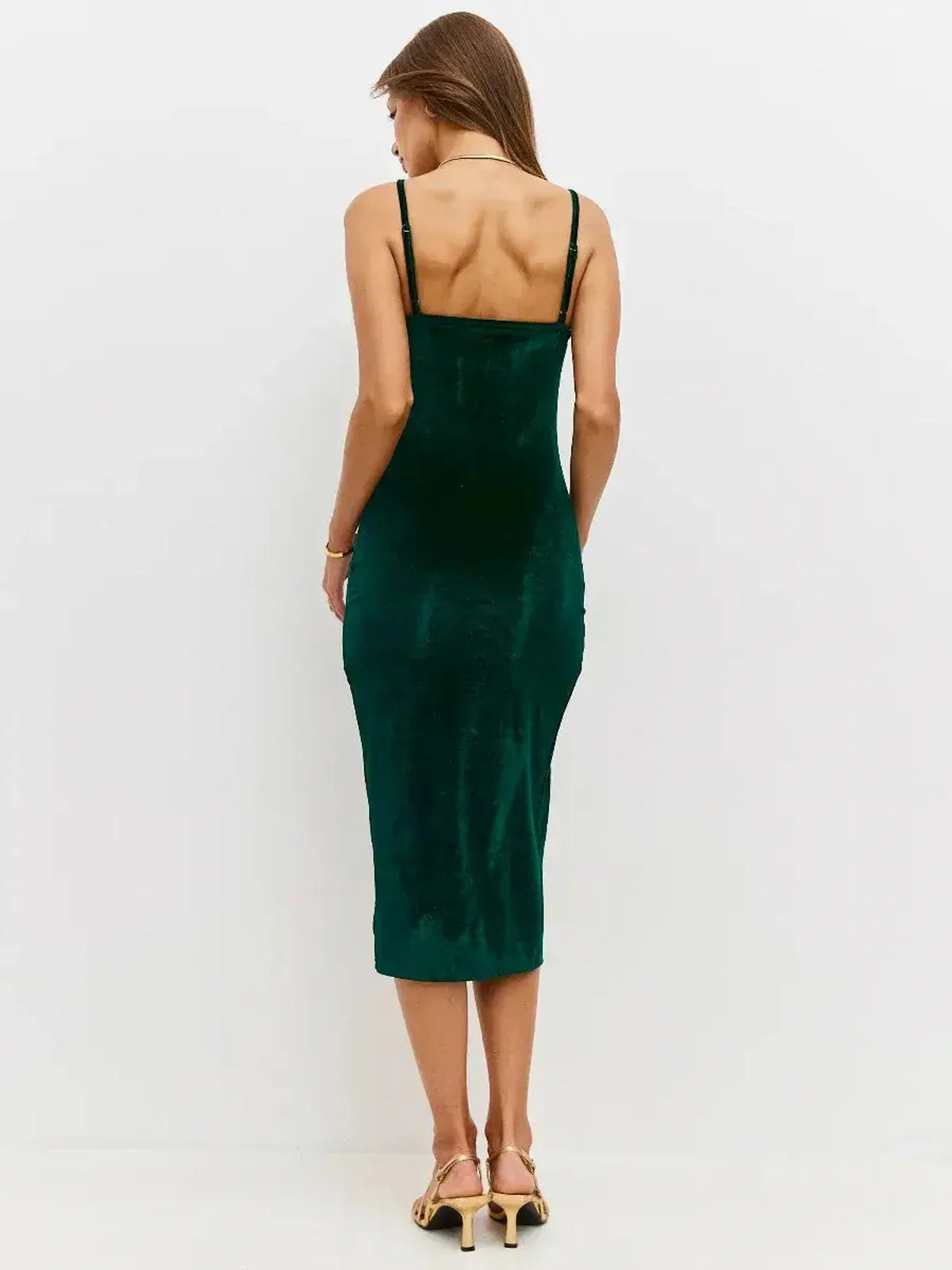 Back view of a woman wearing the Midi Dress Emerald Dusk in rich emerald velvet, showcasing its sleek silhouette and fine straps.