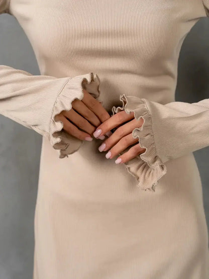 Close-up of hands in beige ribbed dress featuring delicate ruffle accents on sleeves, showcasing modern minimalism.