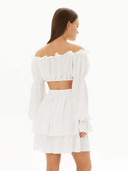 Back view of a woman wearing a chic white ruffle set, featuring an off-shoulder top and layered mini skirt, perfect for summer.