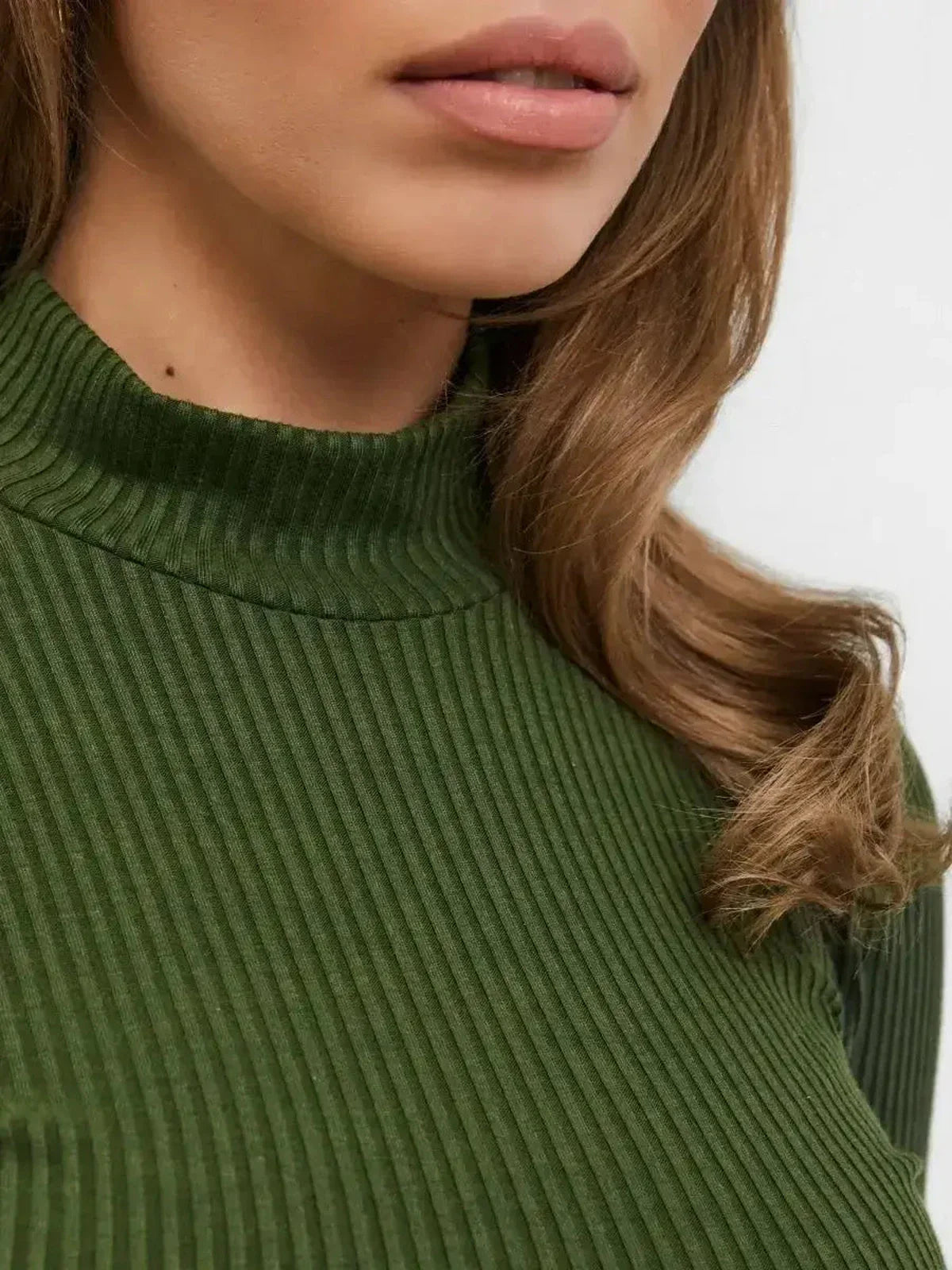 Close-up of a woman's neckline in green ribbed knit, showcasing sleek texture and modern elegance.