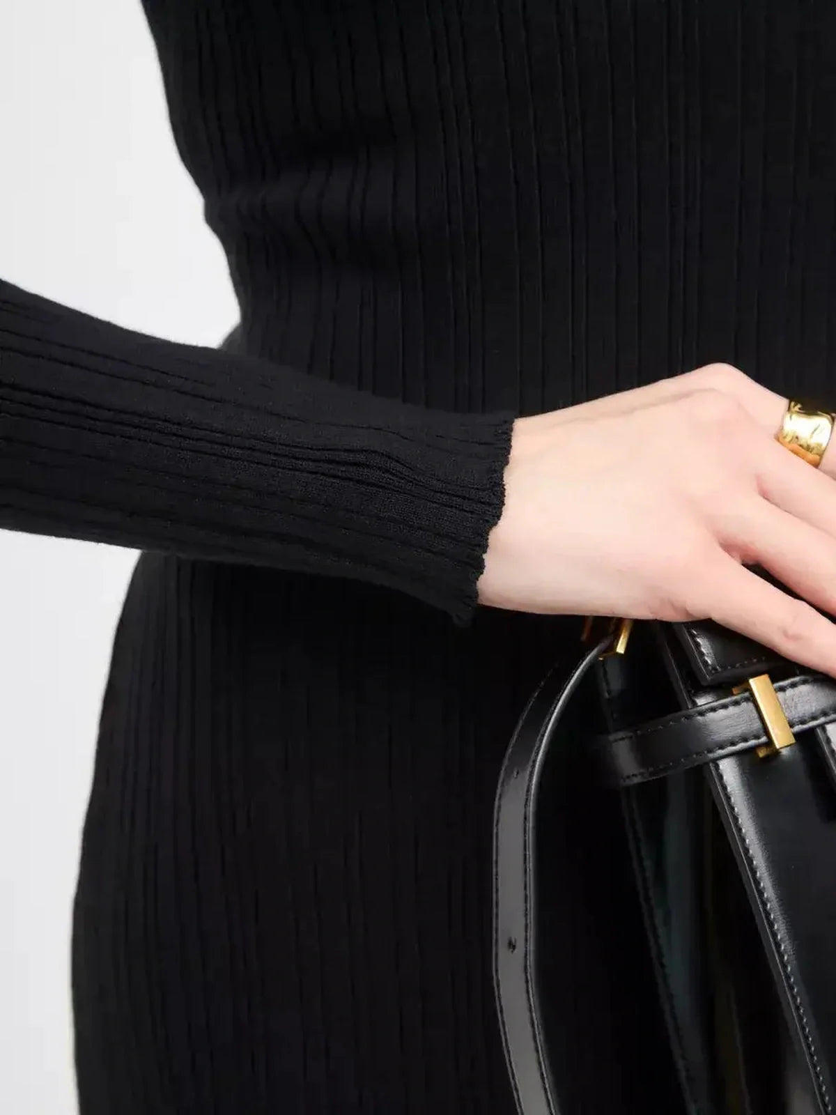 Close-up of a hand holding a black handbag, showcasing the ribbed texture and sleeve detail of the Sculpted Rib Maxi Dress.