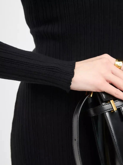 Close-up of a hand holding a black handbag, showcasing the ribbed texture and sleeve detail of the Sculpted Rib Maxi Dress.