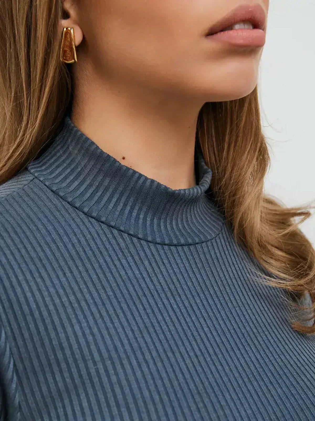Close-up of a woman in a ribbed knit top featuring a mock neck and gold earrings, showcasing a chic and elegant look.