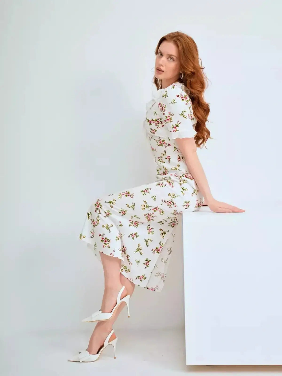 Model wearing the Roselle Midi Dress featuring floral print and ruffle collar, paired with elegant white heels.
