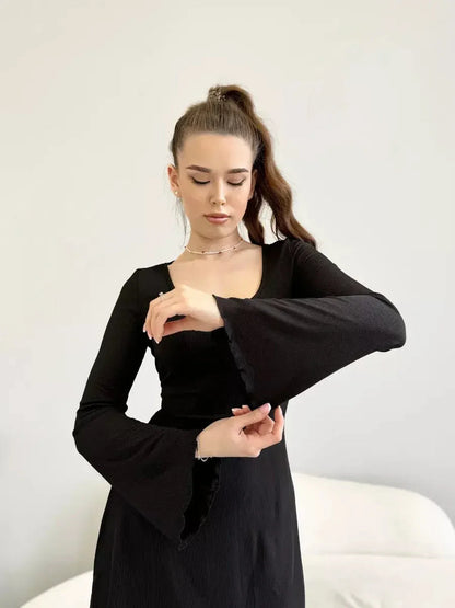 Model showcasing the Noir Flare black dress with flared sleeves and a deep square neckline.