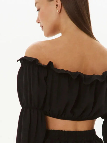 Back view of a woman wearing a black off-shoulder top from the Ruffle Muse Set, showcasing ruffle trim and long sleeves.