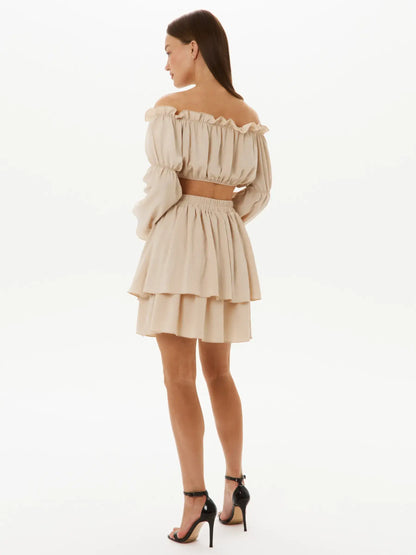 Back view of a model in a Ruffle Breeze Set, showcasing the off-shoulder crop top and tiered skirt in a soft beige tone.