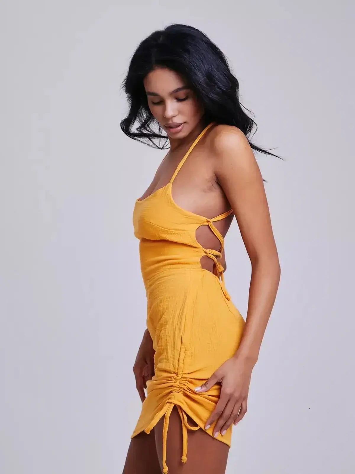 A model showcases the Citrus Rush mini dress in vibrant yellow, featuring a bodycon silhouette and crisscross back straps.
