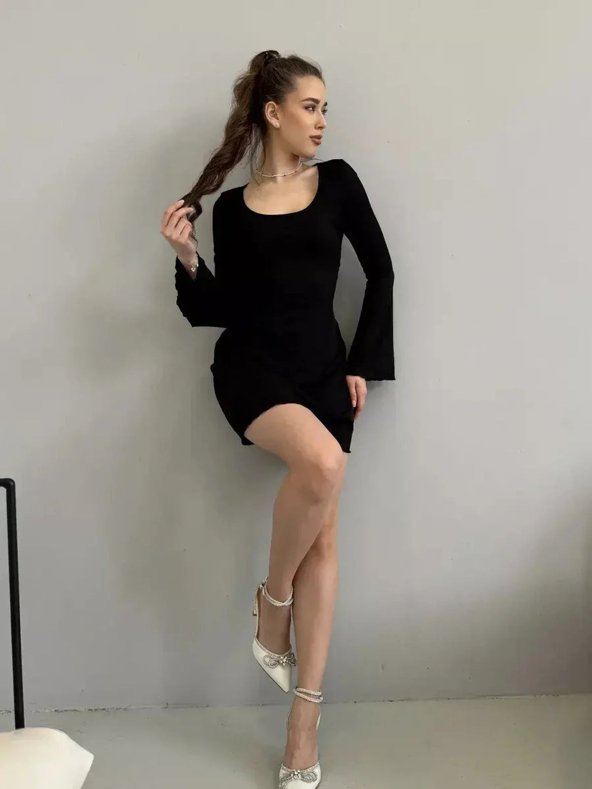 Model showcasing the Noir Flare black mini dress with flared long sleeves and a square neckline, perfect for special occasions.