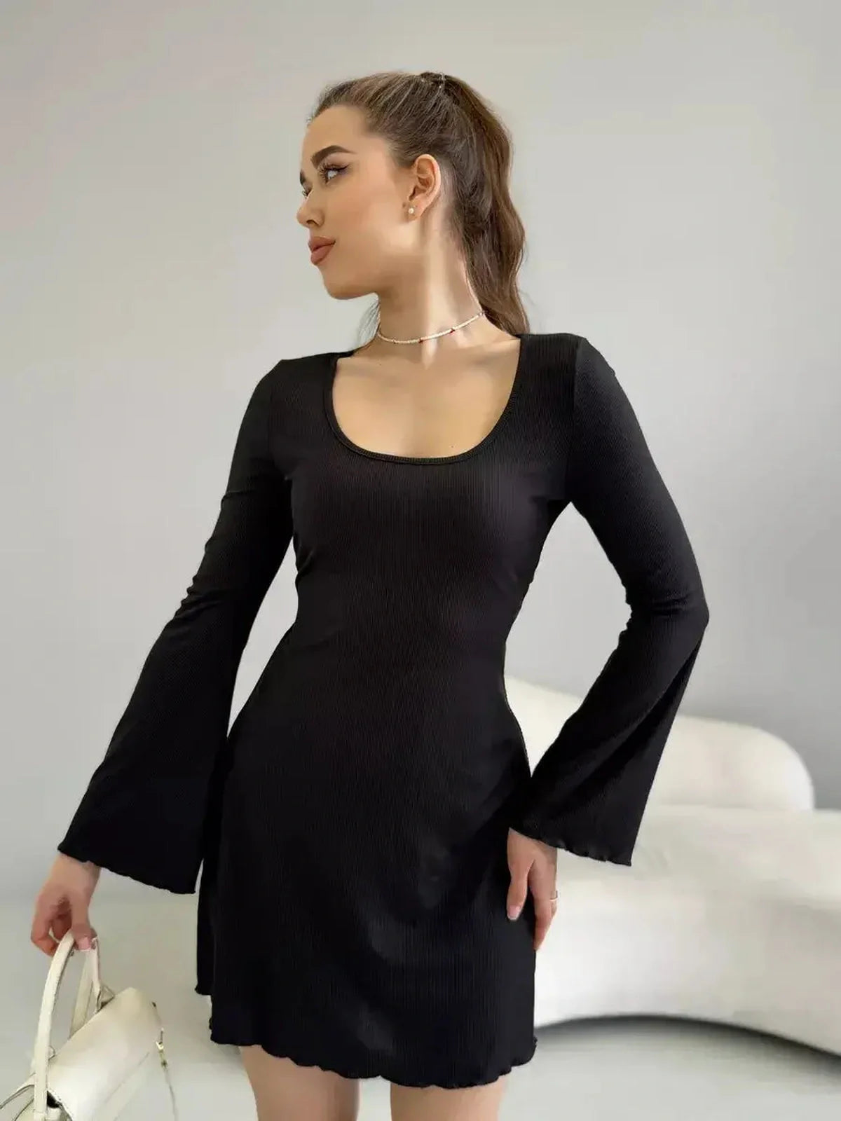 Model in a figure-enhancing black mini dress with long flared sleeves and a deep square neckline.