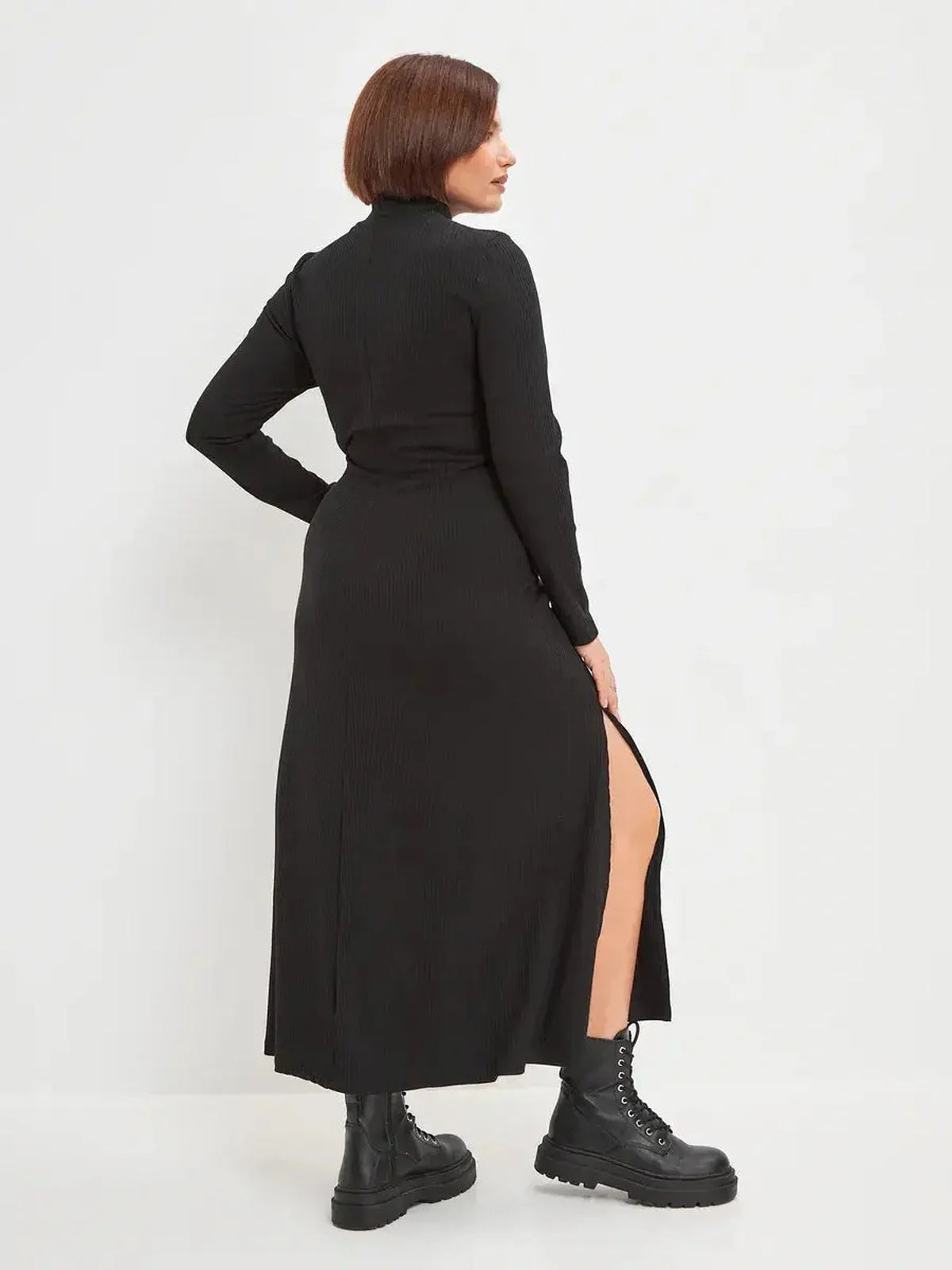 Back view of a black midi dress with side slit, styled with combat boots, showcasing modern elegance for women.