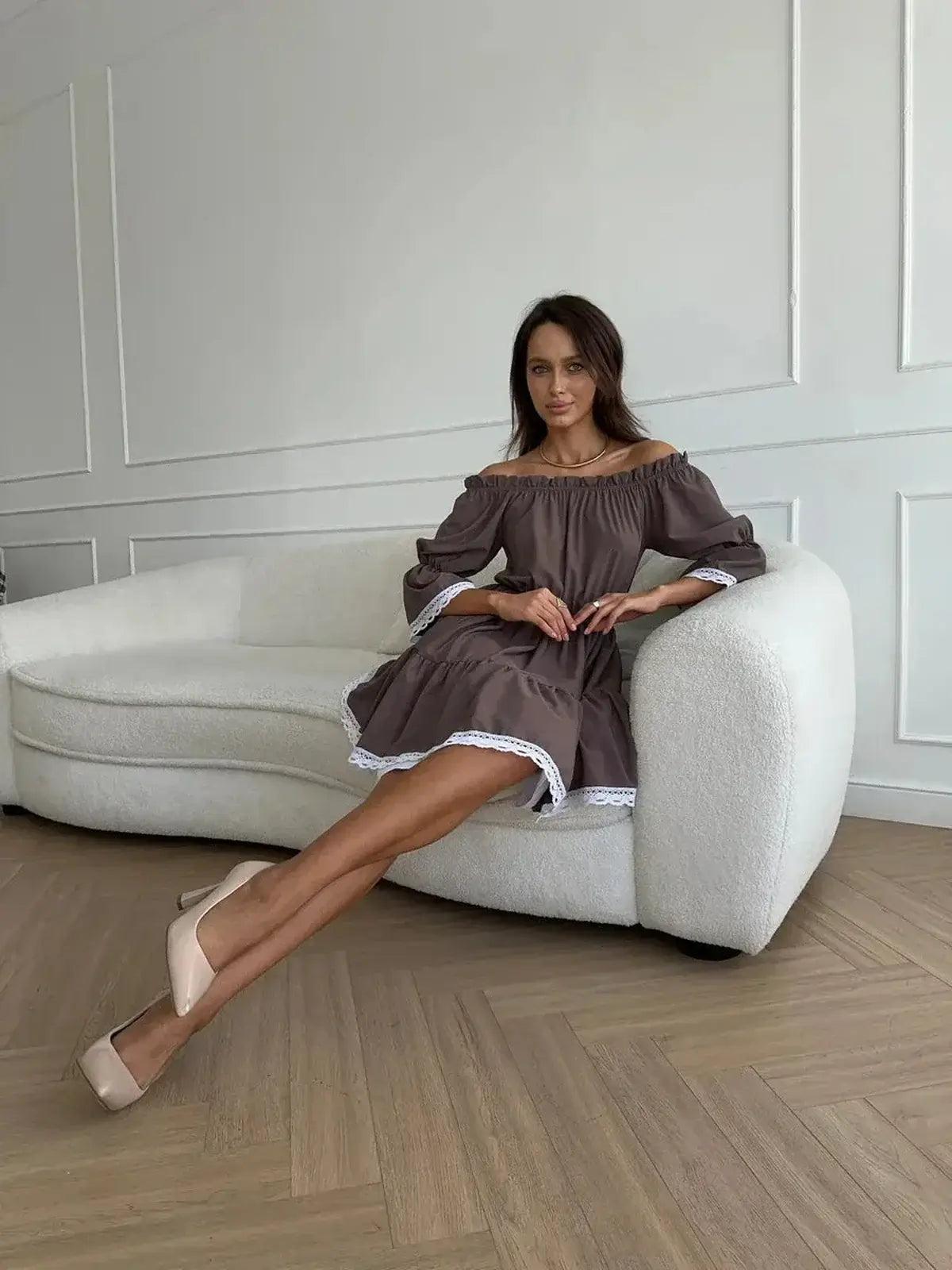 Model wearing the Mocha Muse off-shoulder mini dress, showcasing its elegant brown color and white ruffle trim.