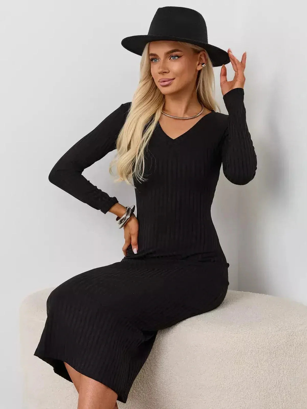 Model wearing a black Muse Midi Dress with a V-neckline and long sleeves, styled with a hat.