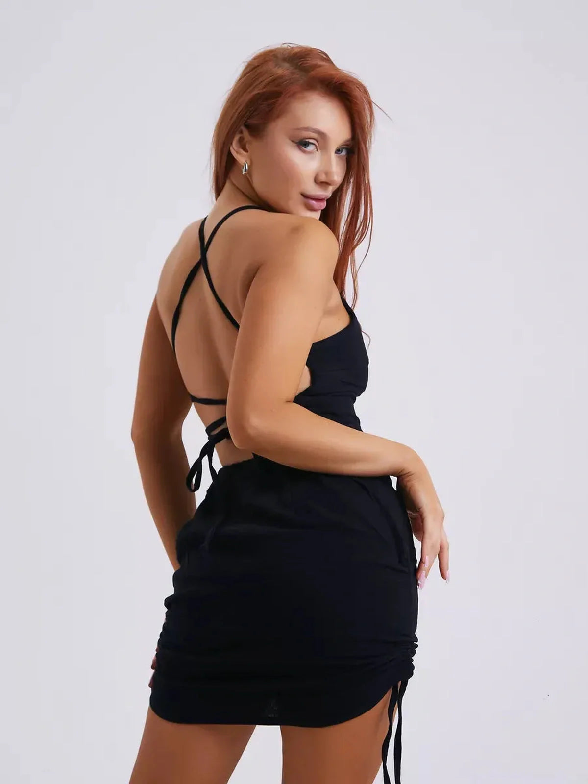 Elegant woman wearing a black Twist Back Muse mini dress with lace-up back and adjustable sides, showcasing summer style.