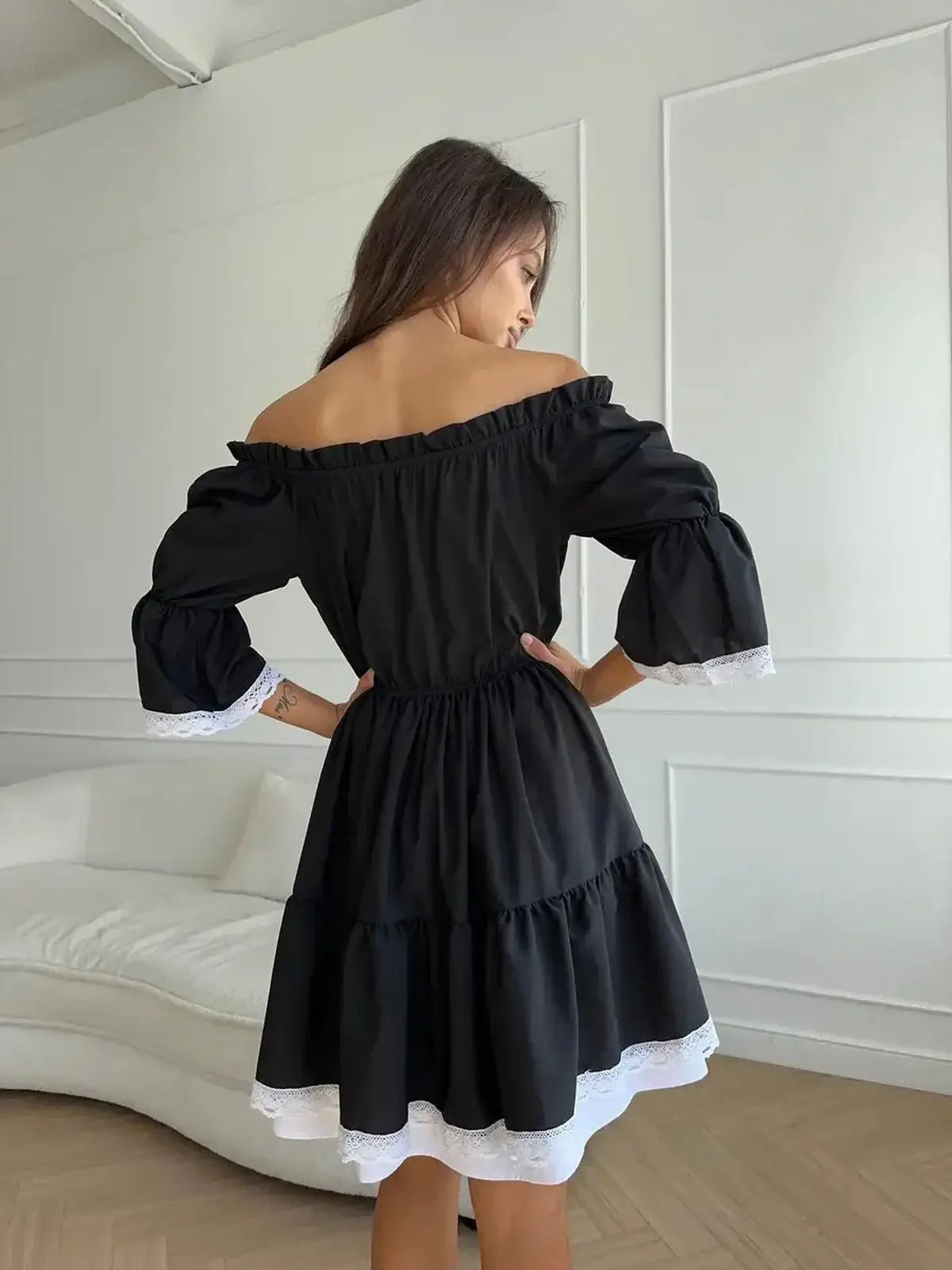 Back view of a romantic black mini dress with off-shoulder neckline, tiered ruffles, and white lace trim.