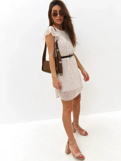 Model wearing an ivory mini dress with polka dots and flutter sleeves, complemented by a black belt and stylish shoes.