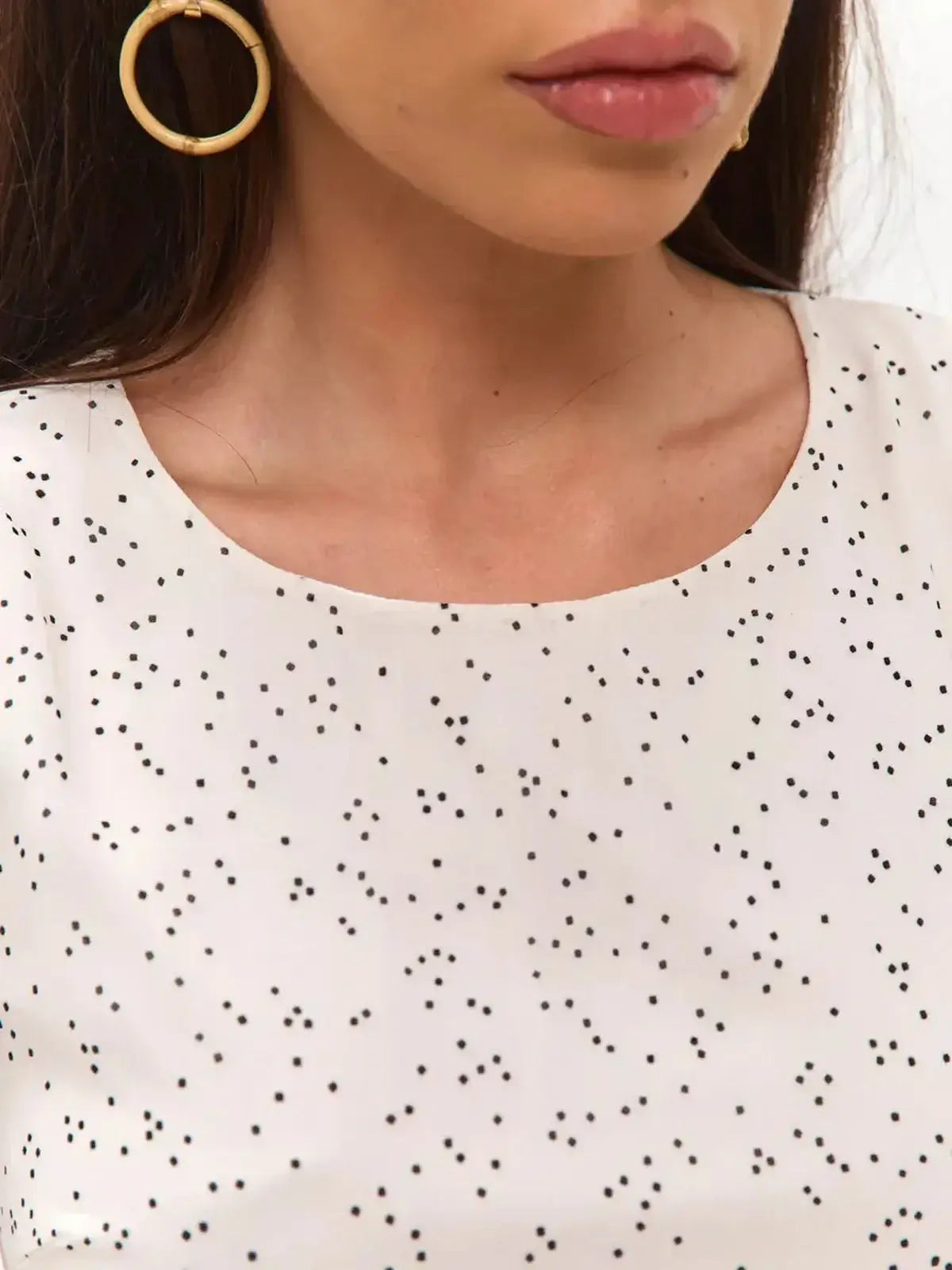 Close-up of a model wearing an ivory polka dot dress, showcasing its round neckline and elegant style.