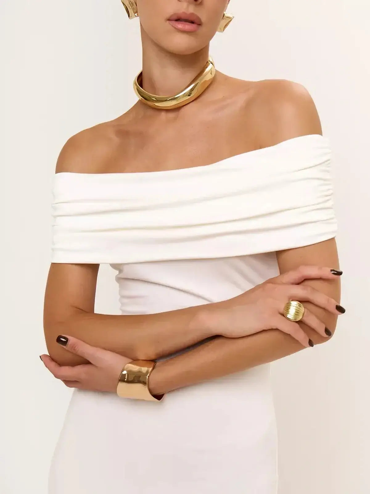 Model wearing an elegant off-shoulder ivory mini dress with ruched detailing and gold accessories.