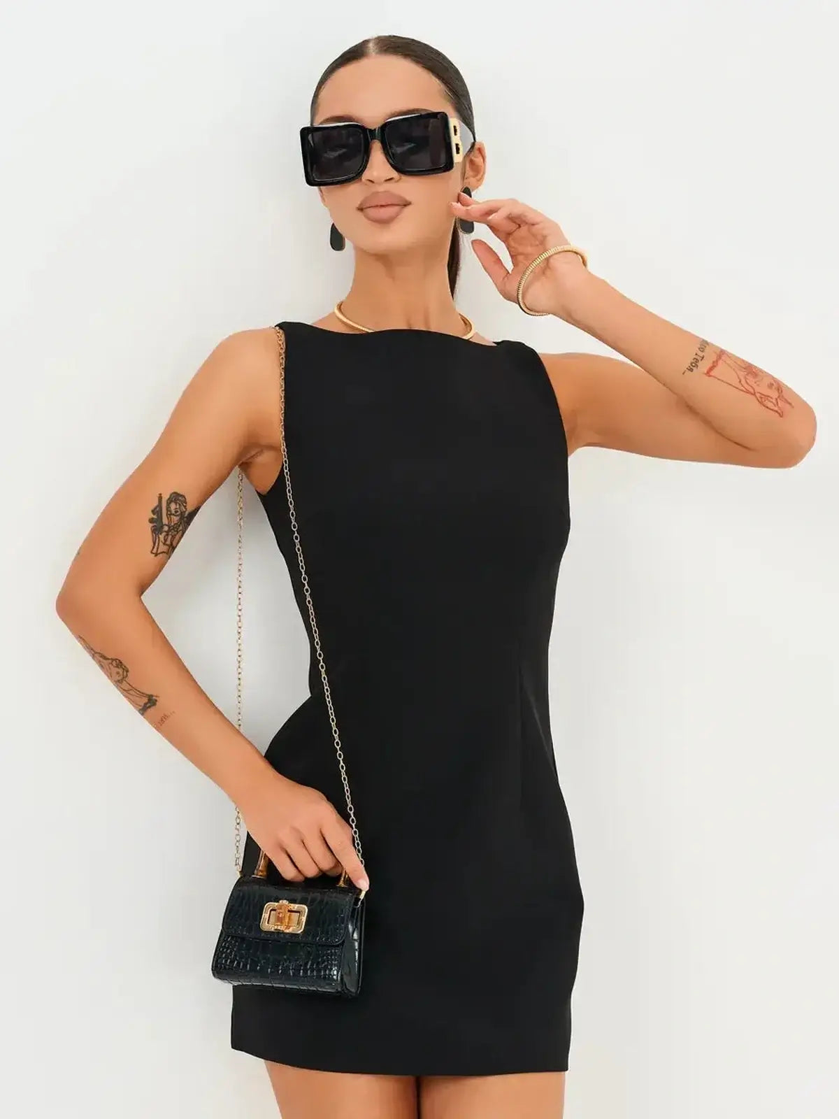 Model in a sleek black Jet Luxe Mini Dress with stylish accessories and oversized sunglasses.