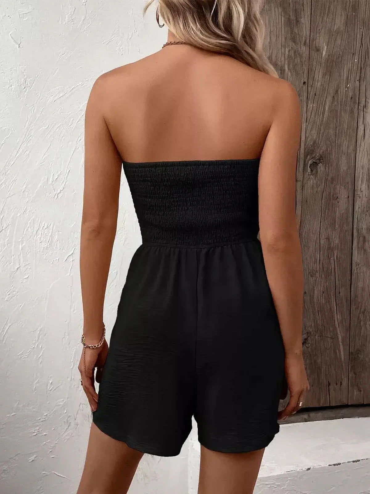 Back view of a woman wearing a Jet Noir Mini Dress, a chic black strapless mini dress with relaxed flared shorts.
