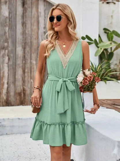 Model in mint green Lace Breeze Mini Dress with lace V-neckline and ruffled hem, accessorized with sunglasses and flowers.