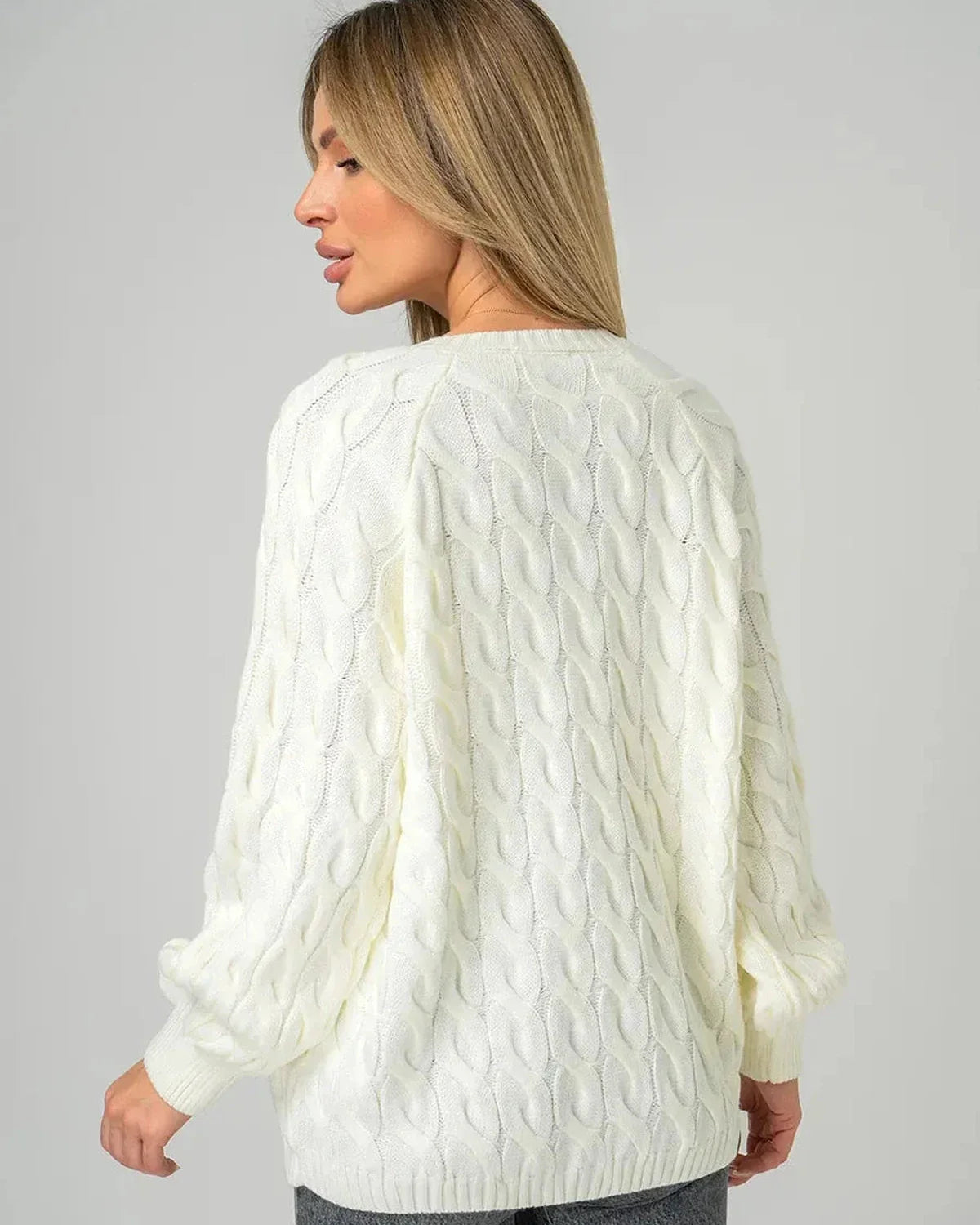 Back view of a woman wearing the Alabaster Sweater by Slimona, showcasing its oversized cream cable knit design.
