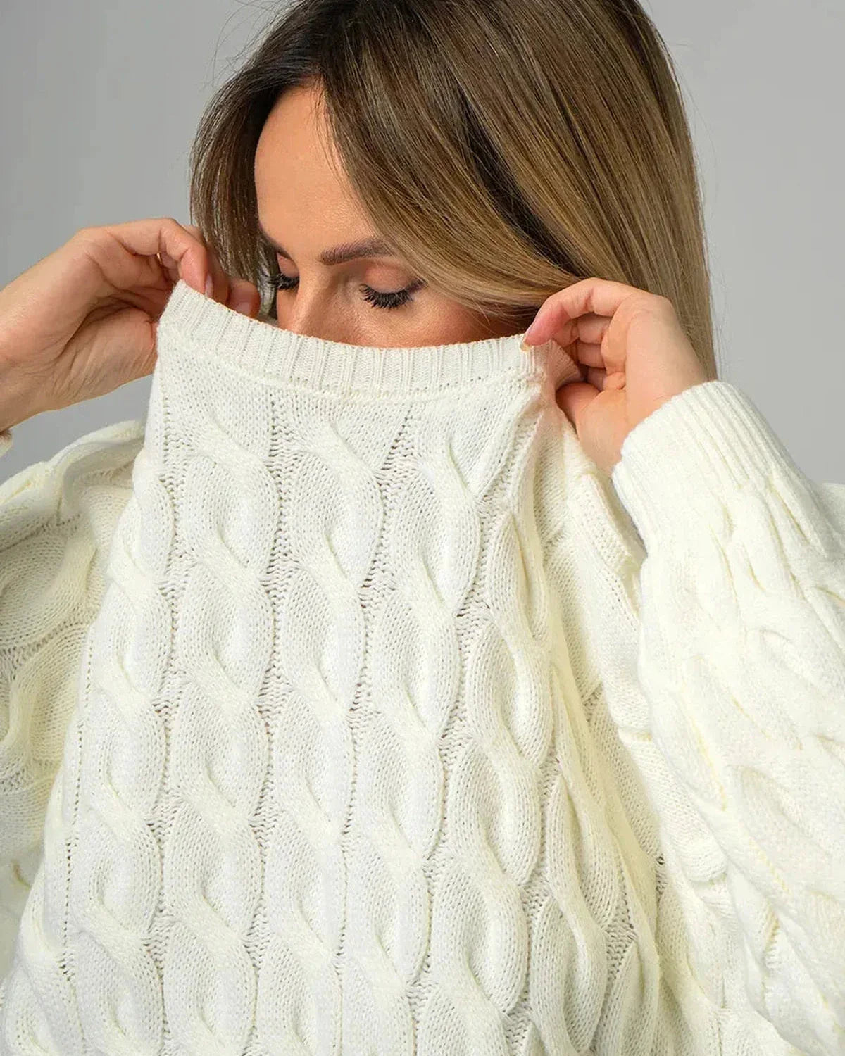 Woman showcasing the Alabaster Sweater by Slimona, an oversized cream cable knit toy, highlighting comfort and elegance.