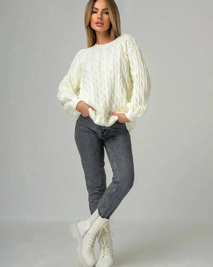 Model wearing the Alabaster Sweater by Slimona, an oversized cream cable knit sweater, paired with stylish grey jeans.