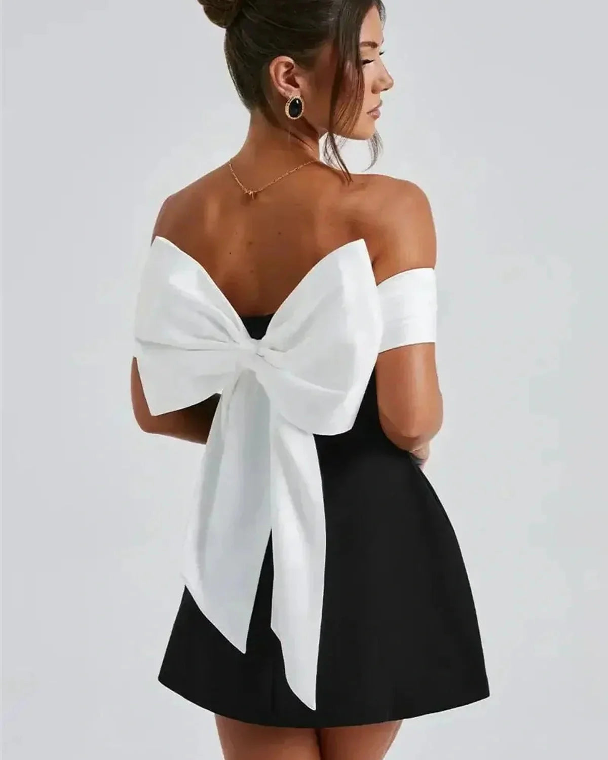 Model showcasing the Alba Mini Dress, featuring an oversized white bow and off-shoulder satin neckline for a chic look.
