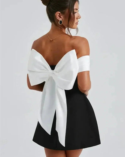 Model showcasing the Alba Mini Dress, featuring an oversized white bow and off-shoulder satin neckline for a chic look.