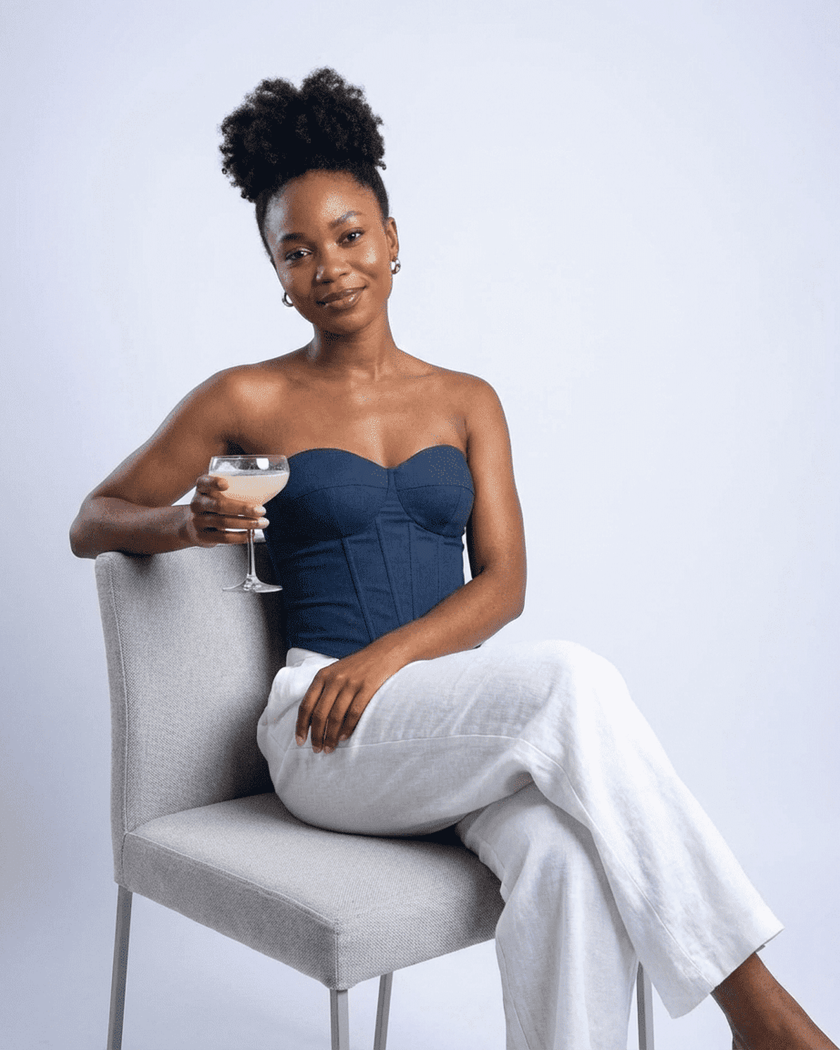 Model wearing the Atlas Corset Top by Slimona, navy faux denim bustier, holding a cocktail, seated elegantly.