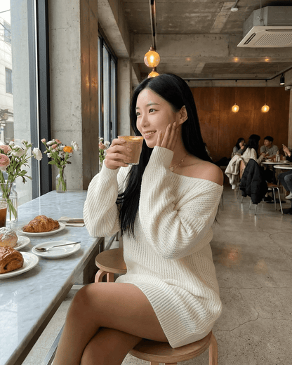 Woman enjoying a beverage in a cafe wearing the Aurora Mini Dress by Slimona, featuring an off-the-shoulder design.